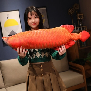 Detailed view of a large orange dragon fish plush pillow held in a cozy home setting