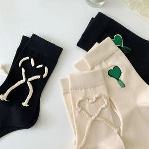 Dettaglio del ricamo a cuore e laccetti con nappe su calze nere e beige neutro