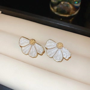 Gros plan de boucles d'oreilles fleurs en émail blanc avec finition dorée perlée