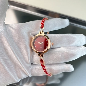 Detailed close-up of a slim red quartz watch with golden bangle and enamel detailing