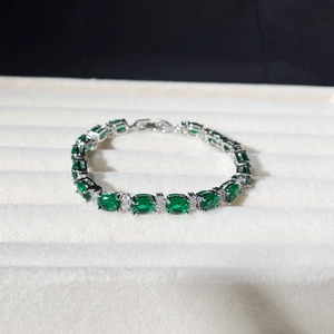 Detail of emerald green oval stones set in silver bracelet inside a white jewelry box