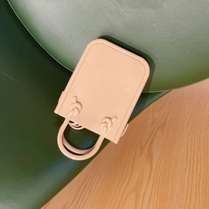 Detail of nude PVC jelly handbag with unique knot handles on a dark green surface