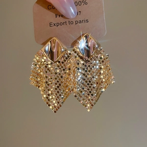 Detailed close-up of golden metal mesh tassel earrings with shimmering fabric-like texture