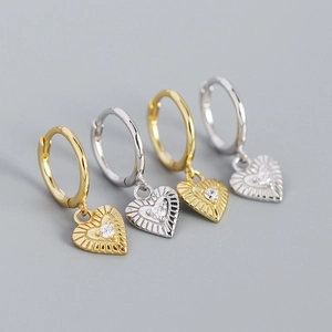 Macro detail of gold and silver heart earrings with radial texture and zircon