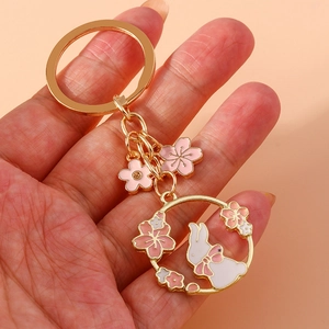 Golden metal keychain with a white rabbit and pink cherry blossoms on pink background