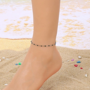 Detailed view of a silver anklet with green beads on a model's ankle at the beach