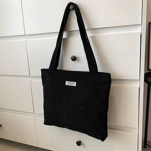 Detail of a black corduroy tote bag with Fashion label hanging on a white cabinet