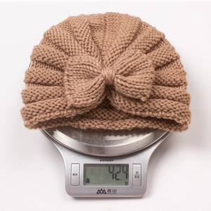 Brown knitted baby hat weighing 42.9g on a digital scale showing quality and weight
