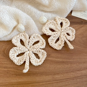 Macro detail of raffia woven clover earrings with handmade straw texture on wood background