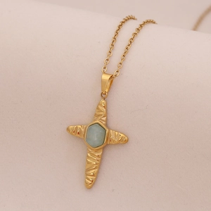 Golden stainless steel necklace with a blue natural stone cross pendant on beige fabric