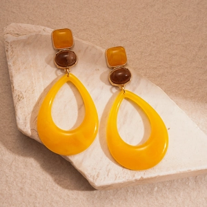 Detail of geometric resin drop earrings featuring yellow and brown stones on stone