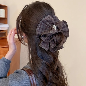Close-up of a brown plaid scrunchie with a minimalist tag on a low ponytail hair style