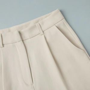 Detail of high-waisted beige suit pants showing front pleats and side pockets