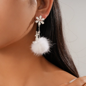 Close-up of snowflake and reindeer earrings with soft white pompom on model