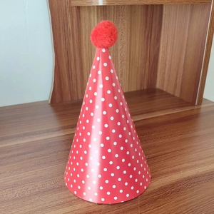 Detail of red party hat with white polka dots and soft pompom on a wooden surface