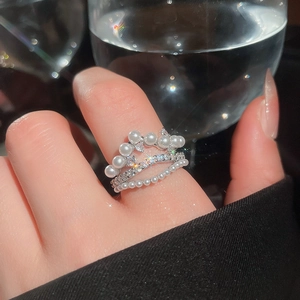 Detail of layered silver rings with crown design featuring pearls and zircon accents