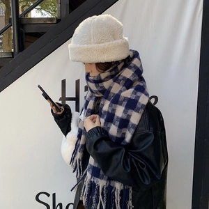 Detail shot of a thick blue checkered scarf and white lamb wool bucket hat on a model