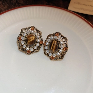 Detailed view of vintage Baroque pearl and tiger eye stud earrings on a ceramic dish