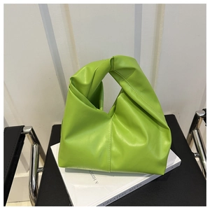 Detail view of a bright green leather knot handbag placed on books on a black chair