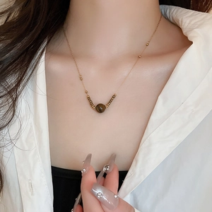 Close-up of a golden beaded necklace featuring a brown tiger eye stone on a model's neck