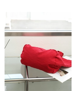 Detail of red washed canvas handbag placed on a glass table next to a magazine