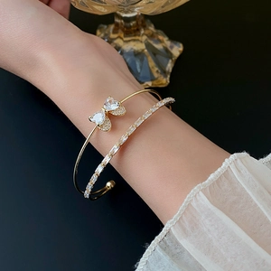 Detailed view of layered gold bow zircon bracelet and diamond-set bangle on wrist