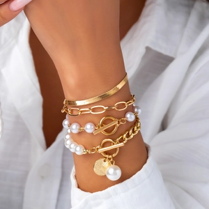 Detail view of a layered gold bracelet set featuring pearls and paperclip chain