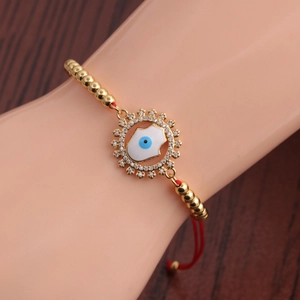 Détail d'un bracelet œil porte-bonheur doré avec cordon rouge et pendentif zircon