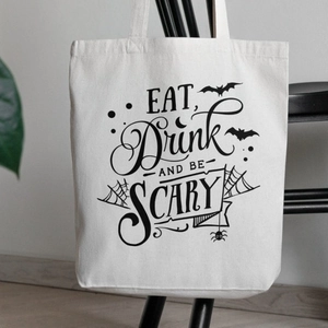 White canvas tote bag with Eat Drink and Be Scary Halloween print hanging on a black chair
