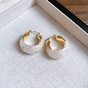 Detailed close-up of retro U-shaped resin earrings in gold and marble white finish