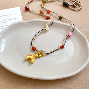 Detail view of a vintage golden horse pendant with colorful beads on a woven necklace cord