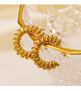 Détail macro des boucles d'oreilles créoles spirales en C plaqué or 18 carats sur verre
