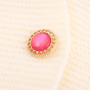 Elegant gold metal button with rose pink resin center on white knit fabric clothing