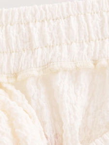 Detail of white cotton linen shorts featuring elastic waistband and pleated texture fabric