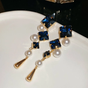 Macro detail of gold earrings with blue crystals, white pearls, and a water drop pendant