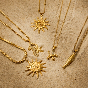Golden stainless steel necklaces set with sun, seahorse, and fish pendants on a sandy beach