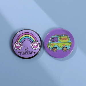 Close-up of purple tinplate badges with be pawsitive text and mystery machine van design