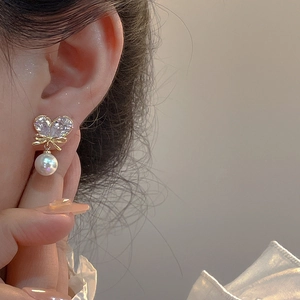 Elegante Ohrringe mit Schleife, herzförmigem Kristall und Perle am Ohr gezeigt