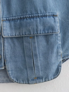 Détail d'une chemise en jean bleu clair avec une grande poche à rabat et coutures jaunes