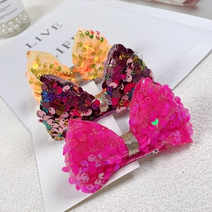 Detailed view of sequin bow hair clips in orange, purple and pink with metal crocodile clips