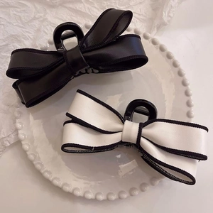 Close-up of elegant black and white bow hair claws with woven edges on a white plate