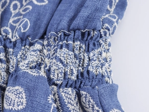 Vue détaillée de la broderie blanche et du smock sur le tissu bleu en coton et lin