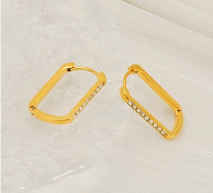 Macro shot of U-shaped gold earrings with paved white zircons on a glass tray
