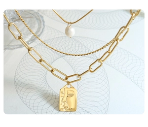 Detail of gold multi-layer chain necklace featuring freshwater pearl and relief pendant