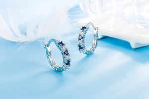 Detail of silver hoop earrings with S925 stamp, blue and white round cut gemstones