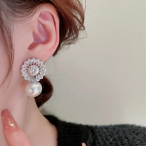 Close-up of zircon flower earrings with white pearl pendants worn by a model