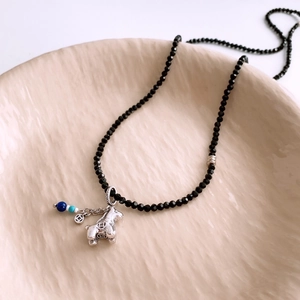 Macro detail of black beaded necklace with silver horse pendant and blue accent beads