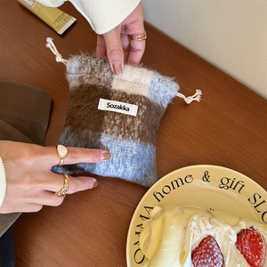 Close-up of soft checkered wool drawstring pouch with a woven brand tag on wooden desk