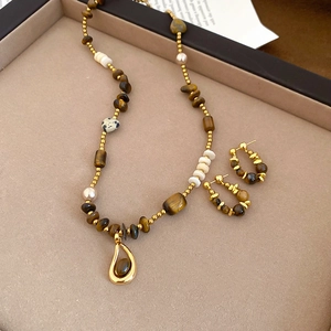 Macro detail of Tiger Eye beaded necklace and matching gold hoop earrings on tray