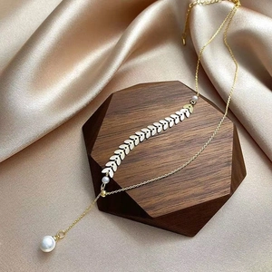 Elegant gold wheat leaf necklace with pearl pendant on champagne silk background